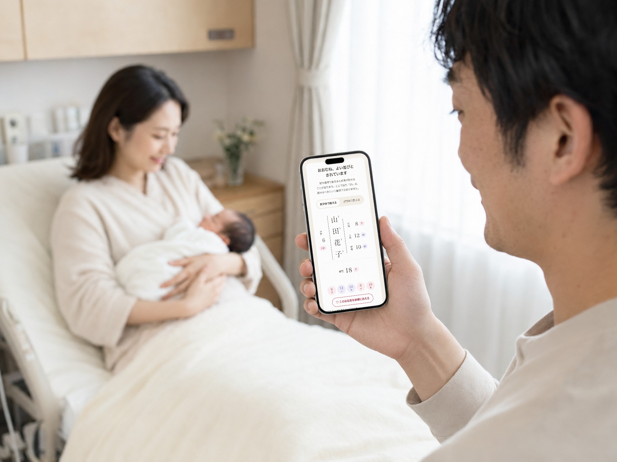 産院の病室で、赤ちゃんを抱く妻のそばで夫がスマートフォンの「なまえのたね」で判定結果を見ている