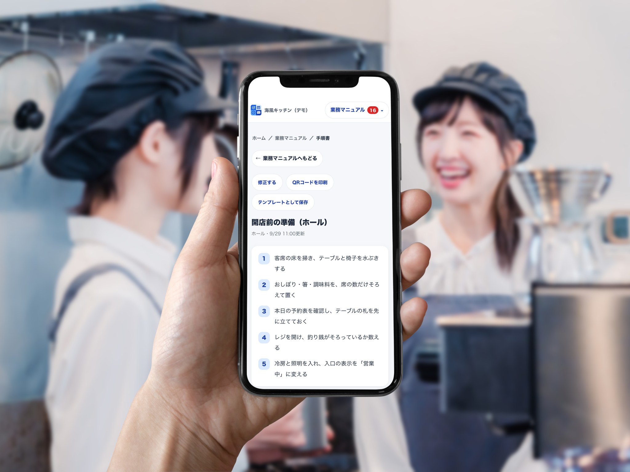 飲食店の厨房で働くスタッフを背景に、スマホに表示した番号つきの業務マニュアル（開店前の準備）
